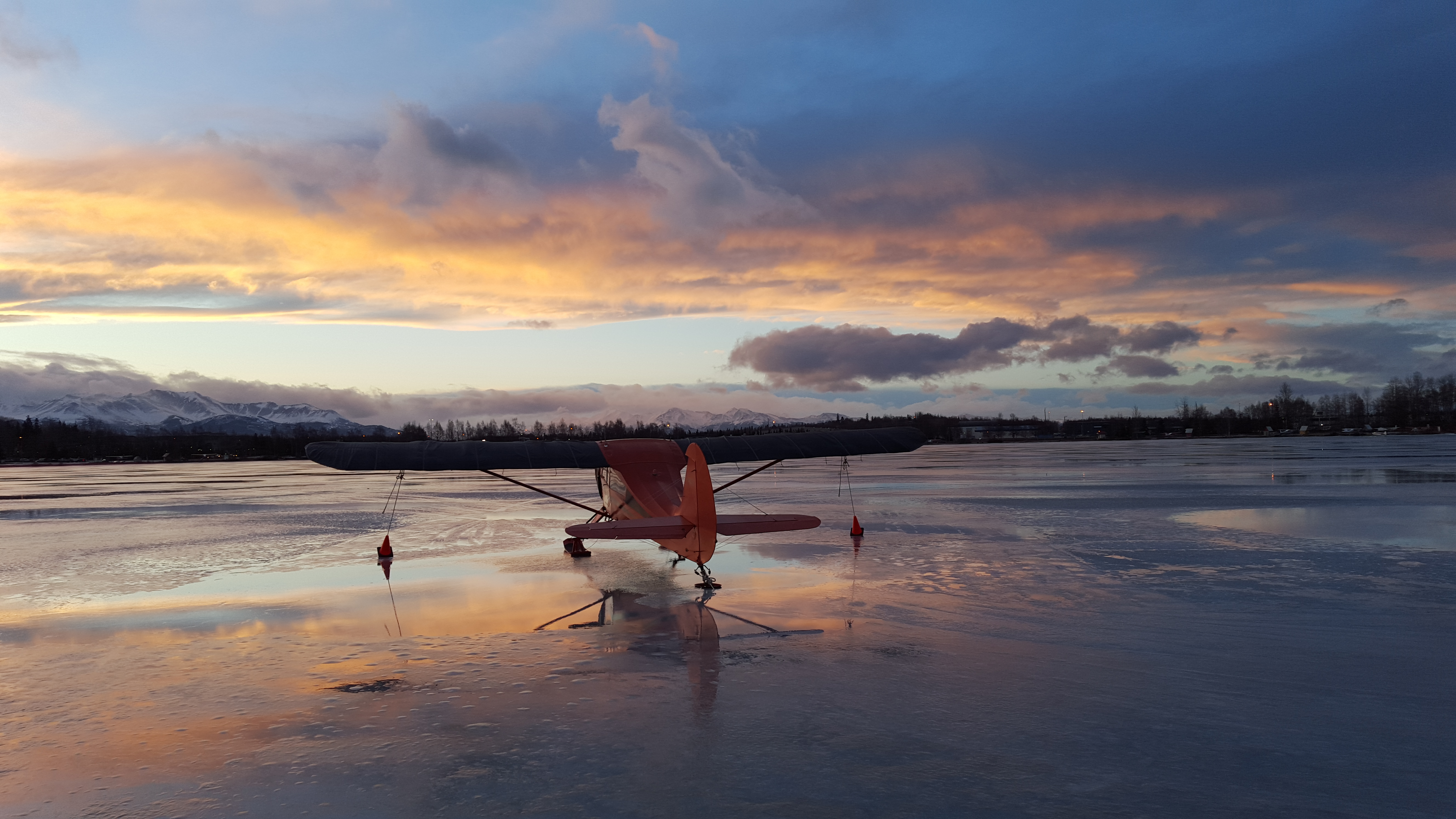 Red and white bush plane on skis reflected on the frozen Lake Hood at sunset in Anchorage, Alaska.